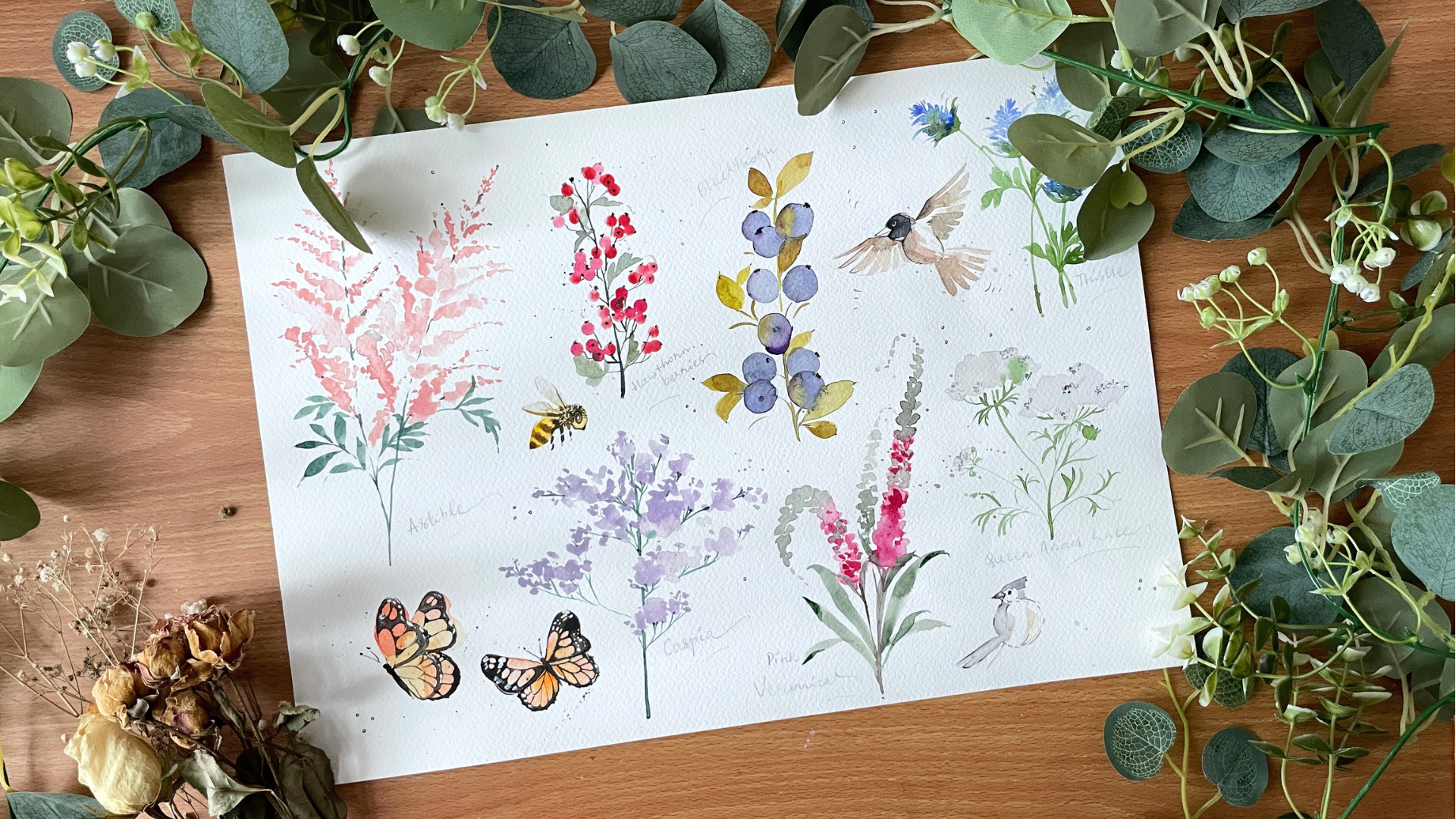 Sheet of floral and butterfly illustrations on a wooden surface with greenery. Femvisionary painting